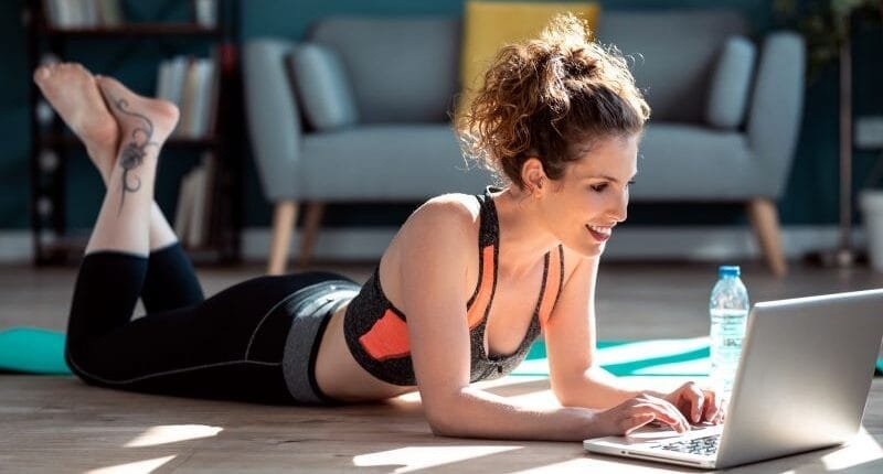 Sporty woman having an online video call via laptop computer while resting in the floor at home.