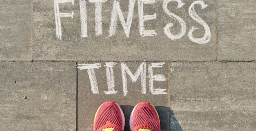Text fitness time written on gray pavement with woman legs in sneakers, view from above